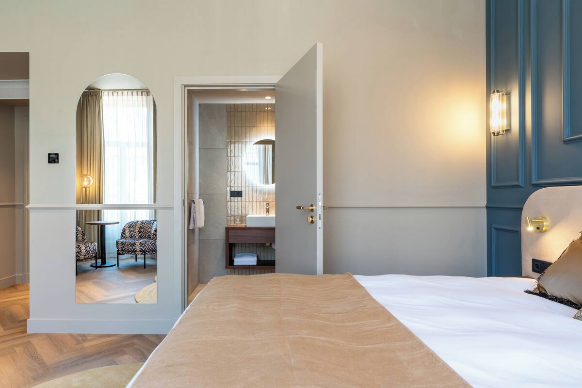 A hotel room with a bed, a bathroom with a mirror, and a seating area with chairs and a table.