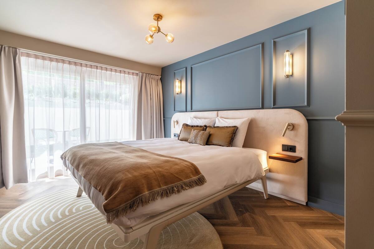 A modern bedroom with a large bed, a bedside table, and a wall-mounted light fixture.