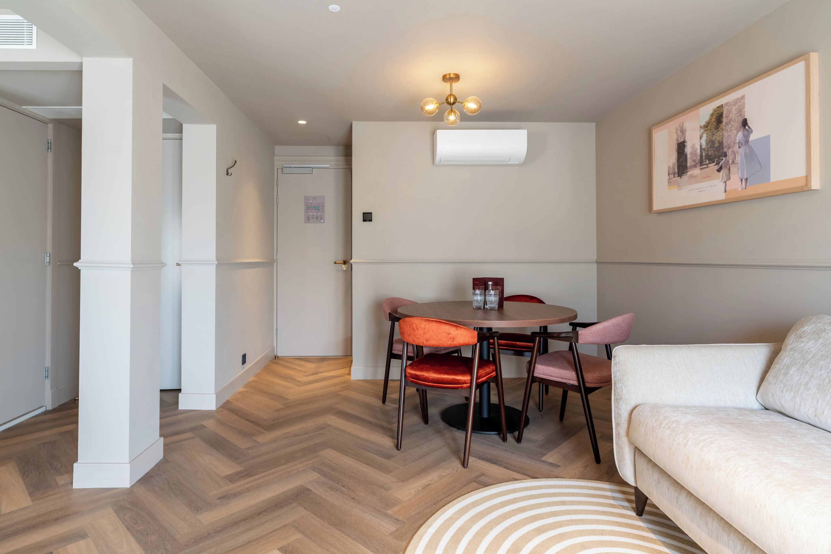 Una sala moderna con un sofá, una mesa de comedor con sillas, un tapete estampado y un aire acondicionado instalado en la pared.