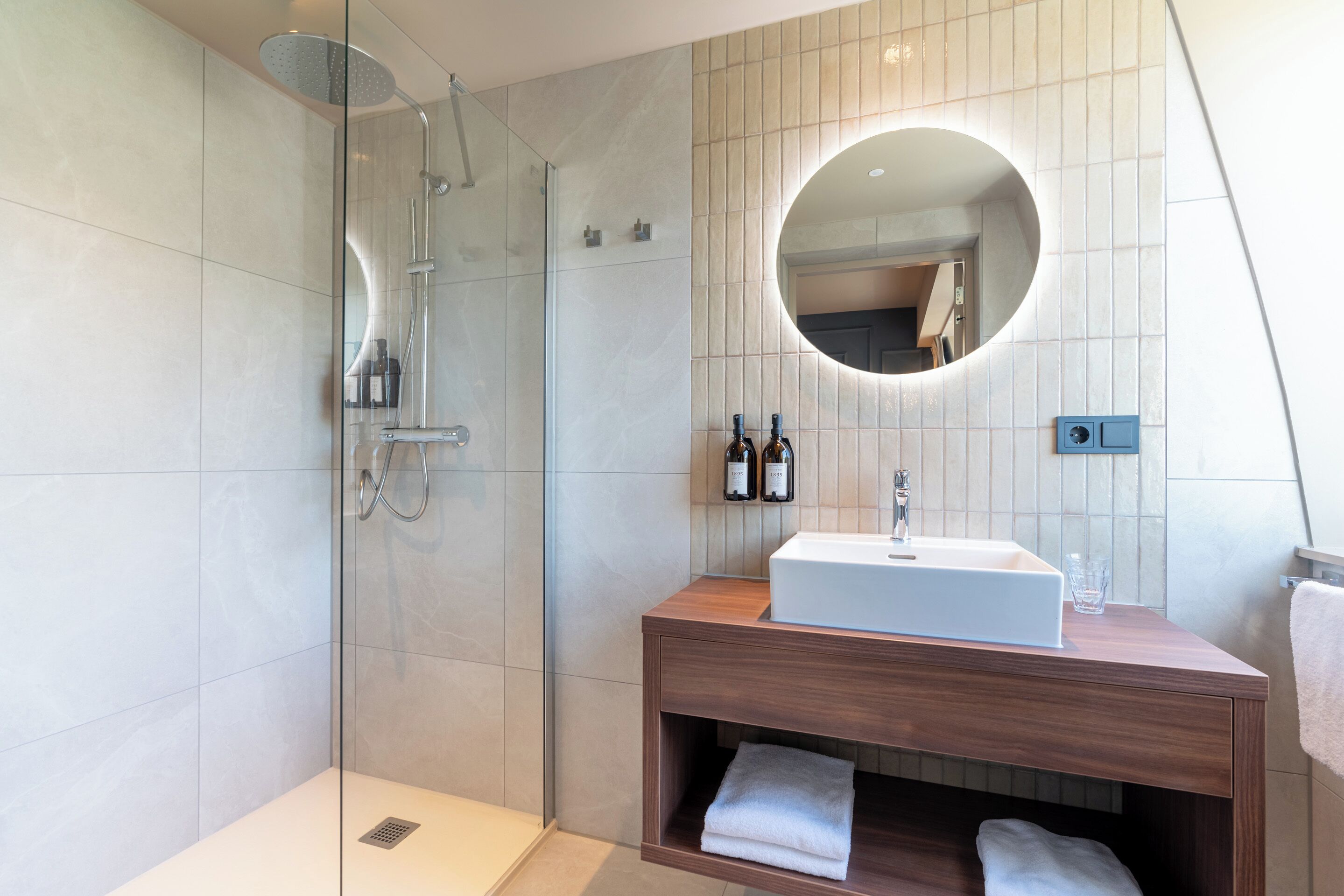 Een moderne badkamer met een douchecabine van glas, een houten wastafelmeubel met een wastafel en een grote spiegel.
