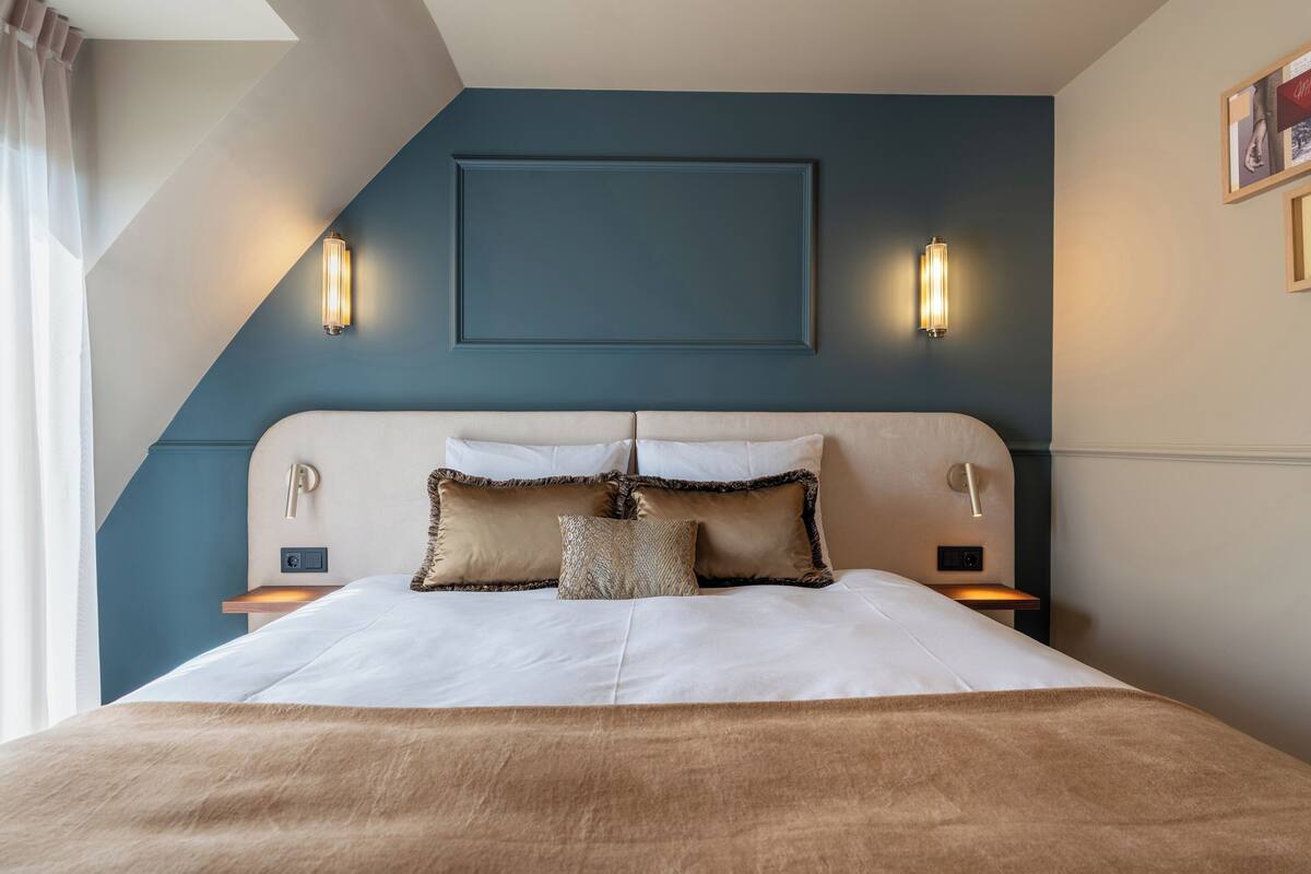 A neatly made bed with a beige and brown blanket, two bedside tables with lamps, and a wall-mounted light fixture.