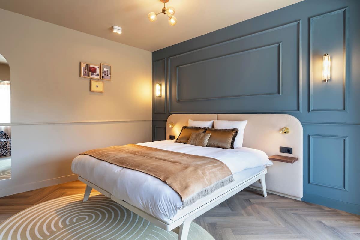 A modern bedroom with a large bed, a bedside table, and a wall-mounted light fixture.