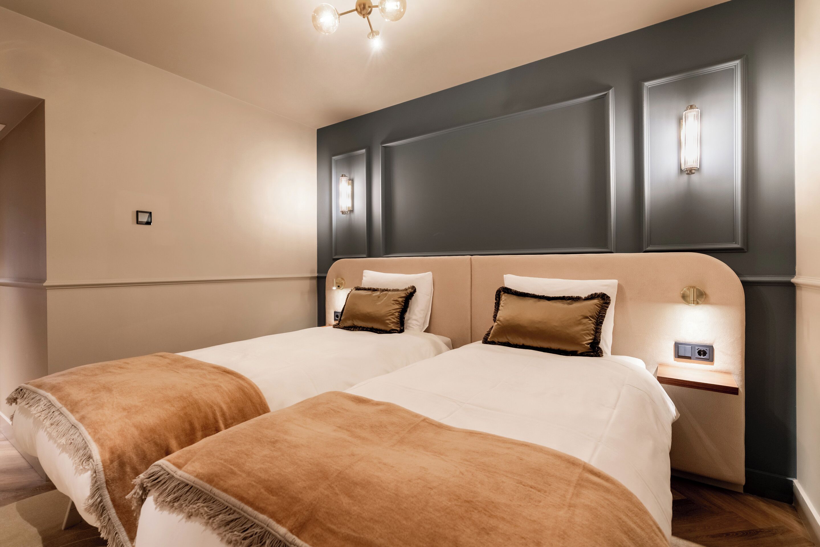 A hotel room with two beds, a dark accent wall, and a small bedside table with a lamp.