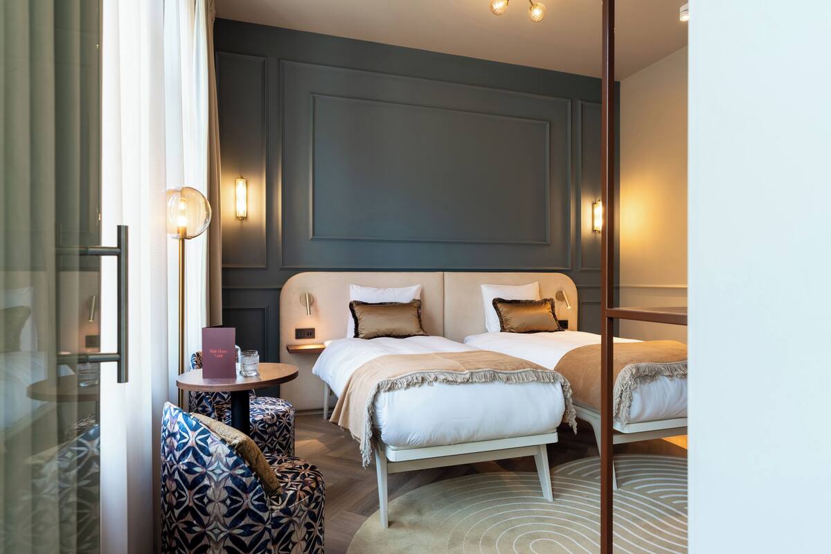 A hotel room with two beds, a small table, and a seating area with patterned chairs.