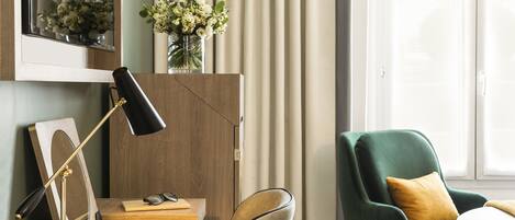 Une pièce avec un bureau en bois, un fauteuil vert, un miroir et un vase rempli de fleurs.