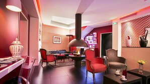 A modern lounge area with a fireplace, red and black furniture, and a bar area in the background. - Hotel Opéra Opal (Paris)