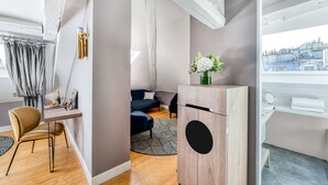 A modern living room with a wooden cabinet, a blue sofa, a dining table with a chair, and a patterned rug. - Hotel Opéra Opal (Paris)