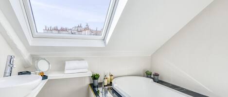 A modern bathroom with a skylight, a freestanding bathtub, a vanity with a sink, and a small potted plant.