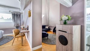 A modern room with a wooden floor, a sofa, a chair, a desk, and a cabinet with a vase of flowers. - Hotel Opéra Opal (Paris)