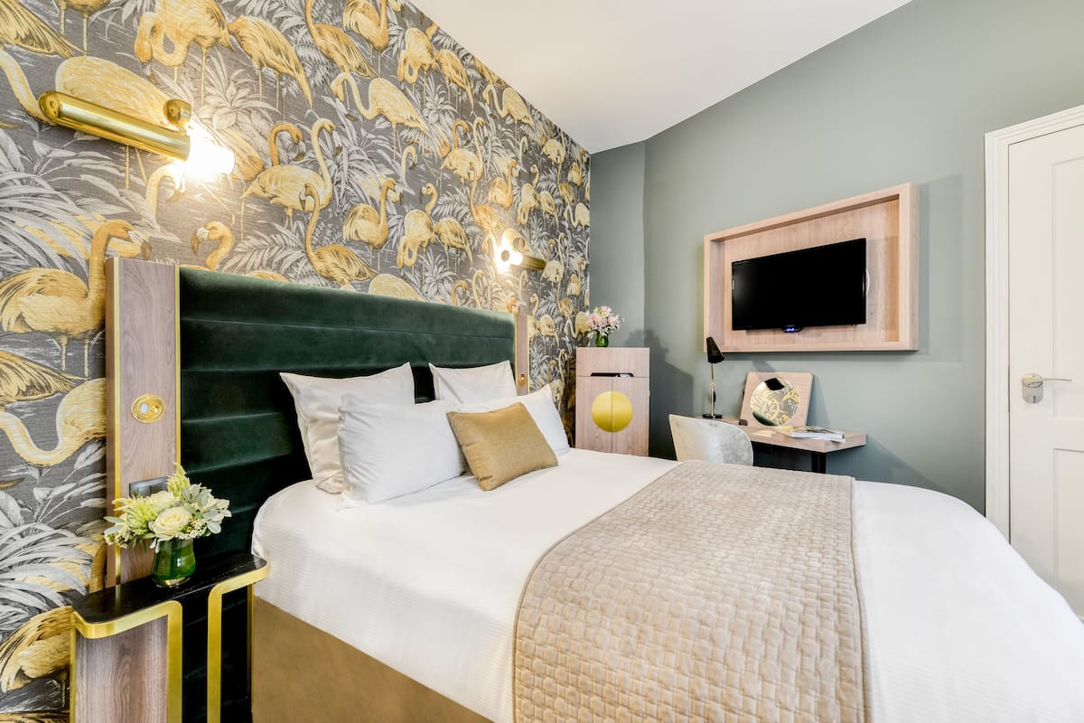 A bedroom with a green upholstered headboard, a flat-screen TV mounted on the wall, and a floral wallpaper design.