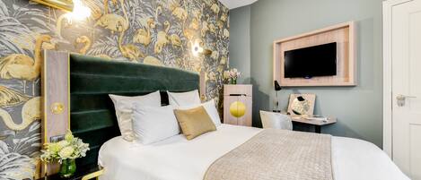 A bedroom with a green upholstered headboard, a flat-screen TV mounted on the wall, and a floral wallpaper design.