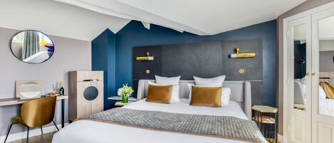 A modern hotel room with a large bed, a desk, a chair, a round mirror, and a wardrobe.