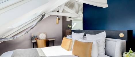 Una habitación de hotel moderna con una cama grande, una mesita con una botella y vasos, una mesita de noche y vistas al cielo a través de una ventana.