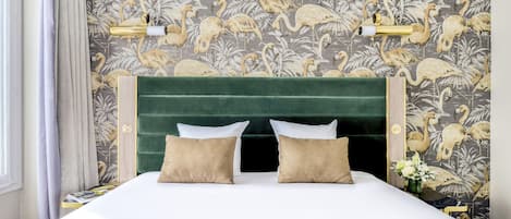 A bed with a green upholstered headboard, two pillows, and a floral wallpaper pattern.