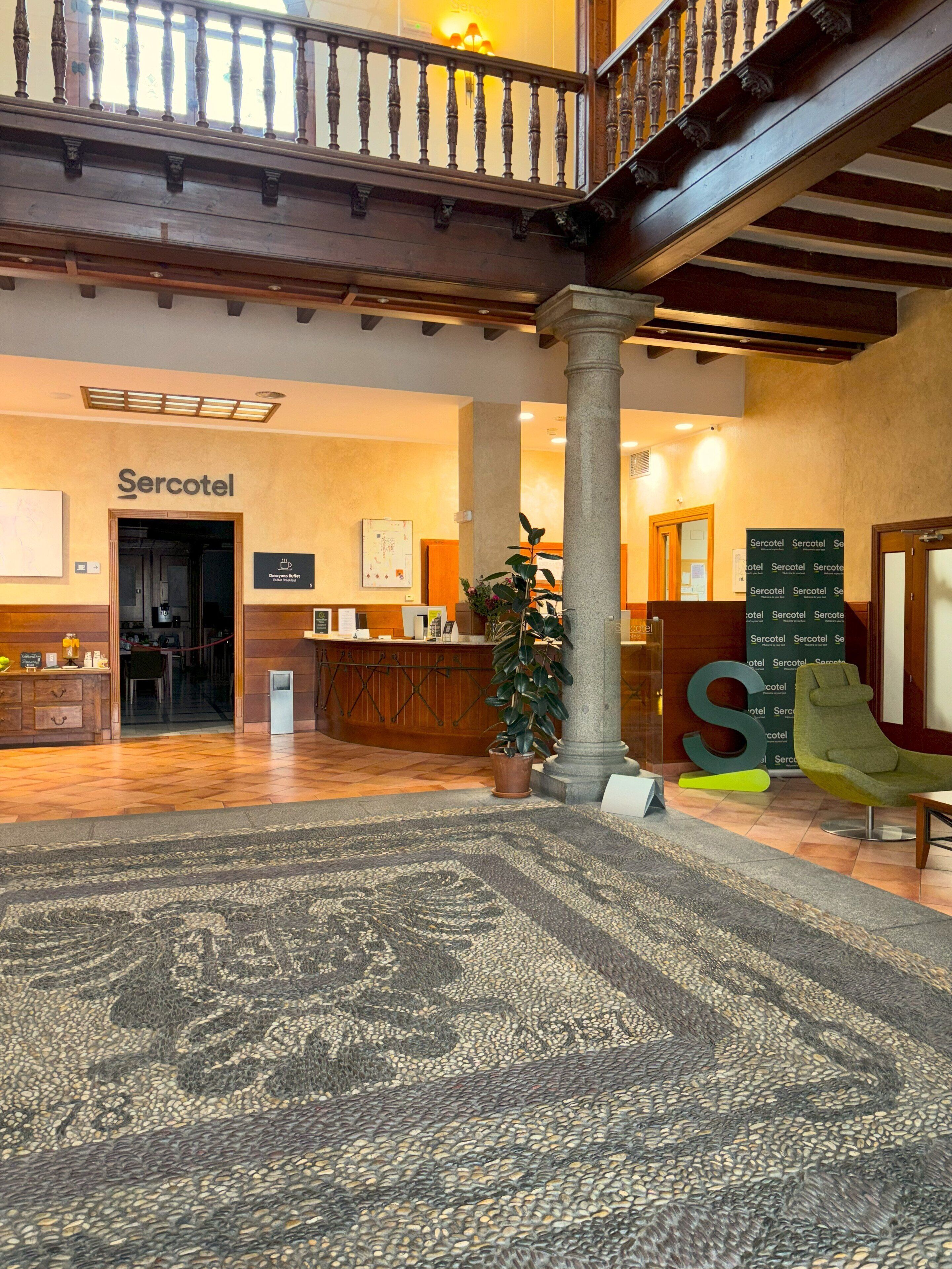 A spacious lobby with a reception desk, a large S-shaped sculpture, and a staircase leading to an upper level.