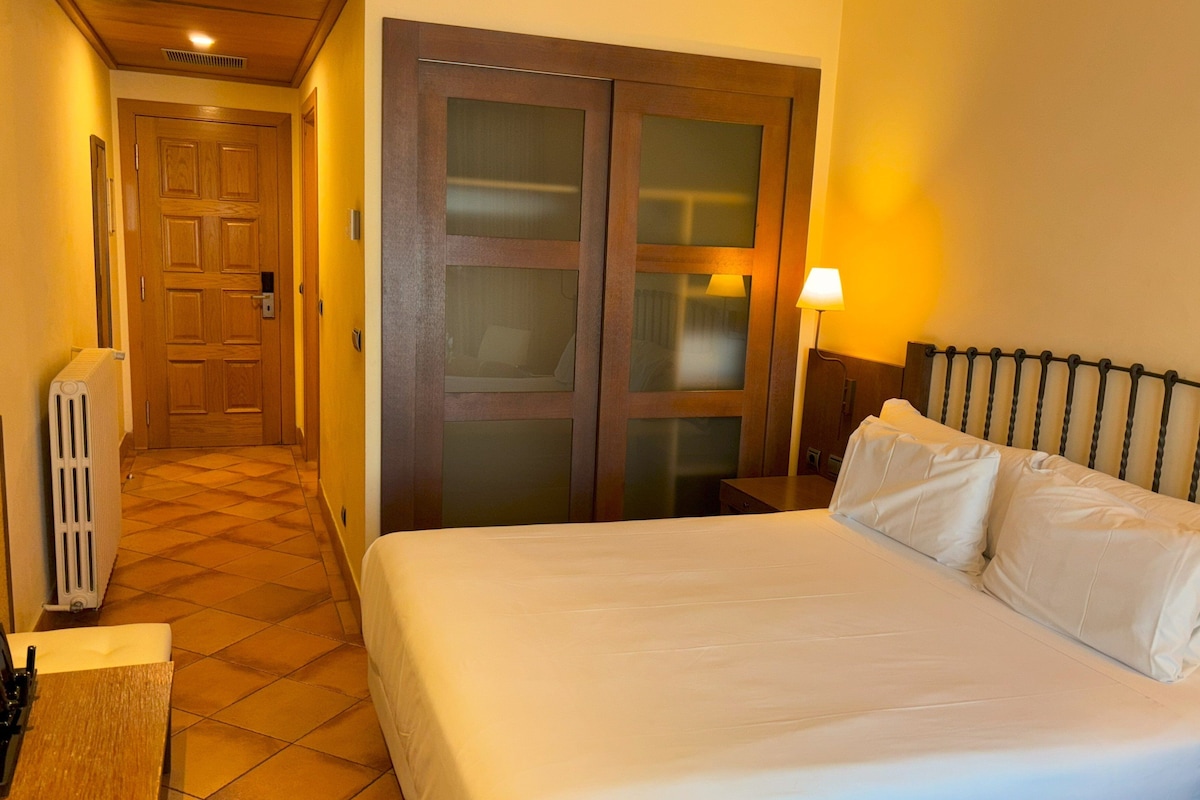 A hotel room with a bed, a radiator, a door, and a lamp.