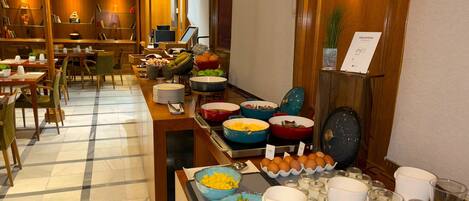 A buffet setup with various food items and beverages, including bowls of fruits, eggs, and a selection of drinks.
