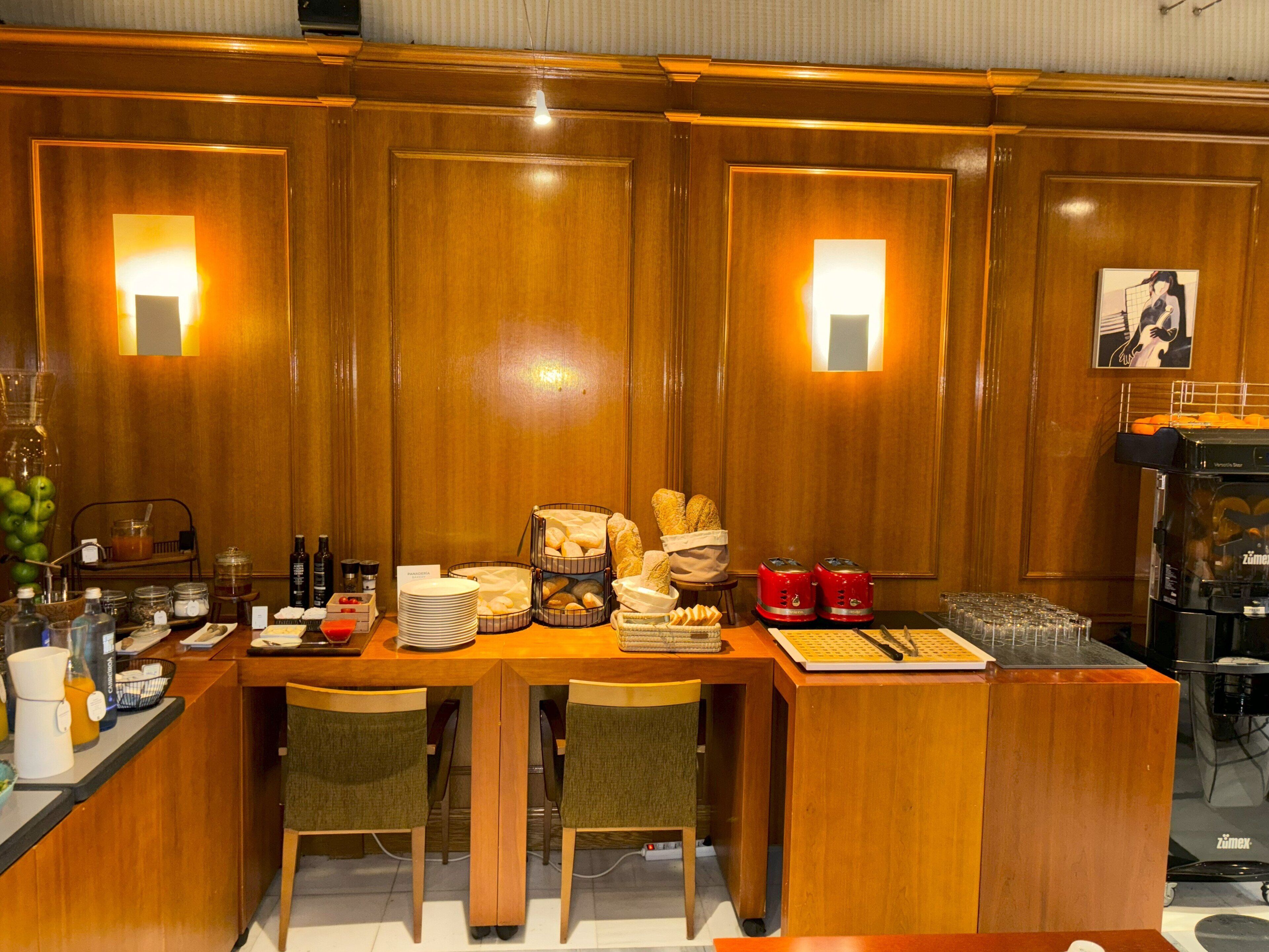 A wooden bar area with a buffet setup, including bread, pastries, and beverages.