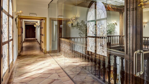 Un pasillo con suelo de baldosas, puertas de cristal y una escalera con barandillas ornamentadas.