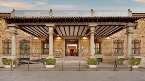 Un edificio histórico con fachada de piedra, un acceso cubierto con columnas y un cartel que dice 