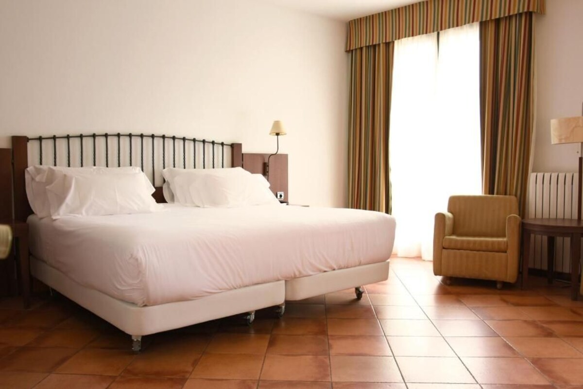 A hotel room with a large bed, a chair, a nightstand, and a lamp.