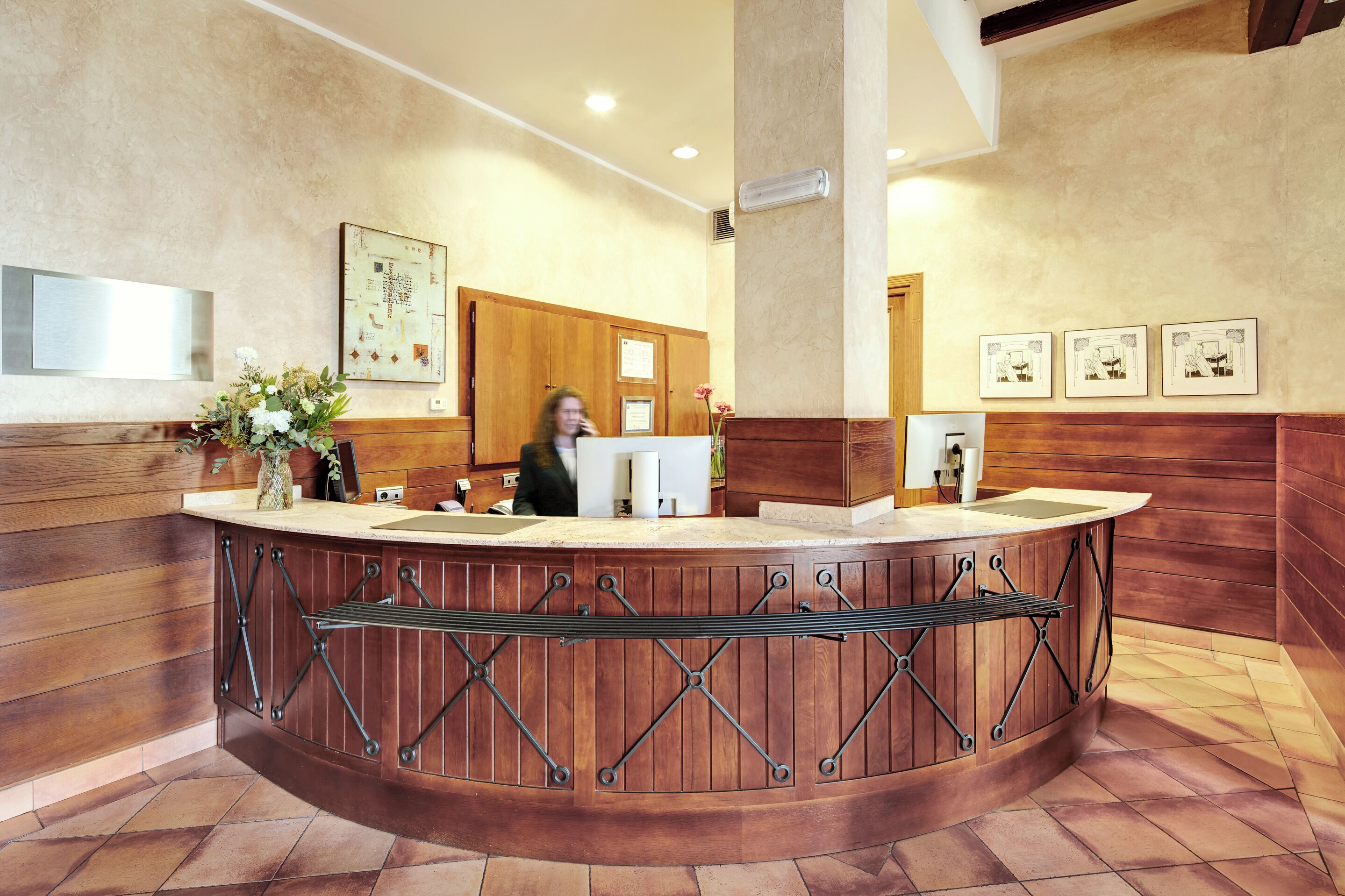 A reception area with a wooden counter, a vase with flowers, and framed pictures on the wall.