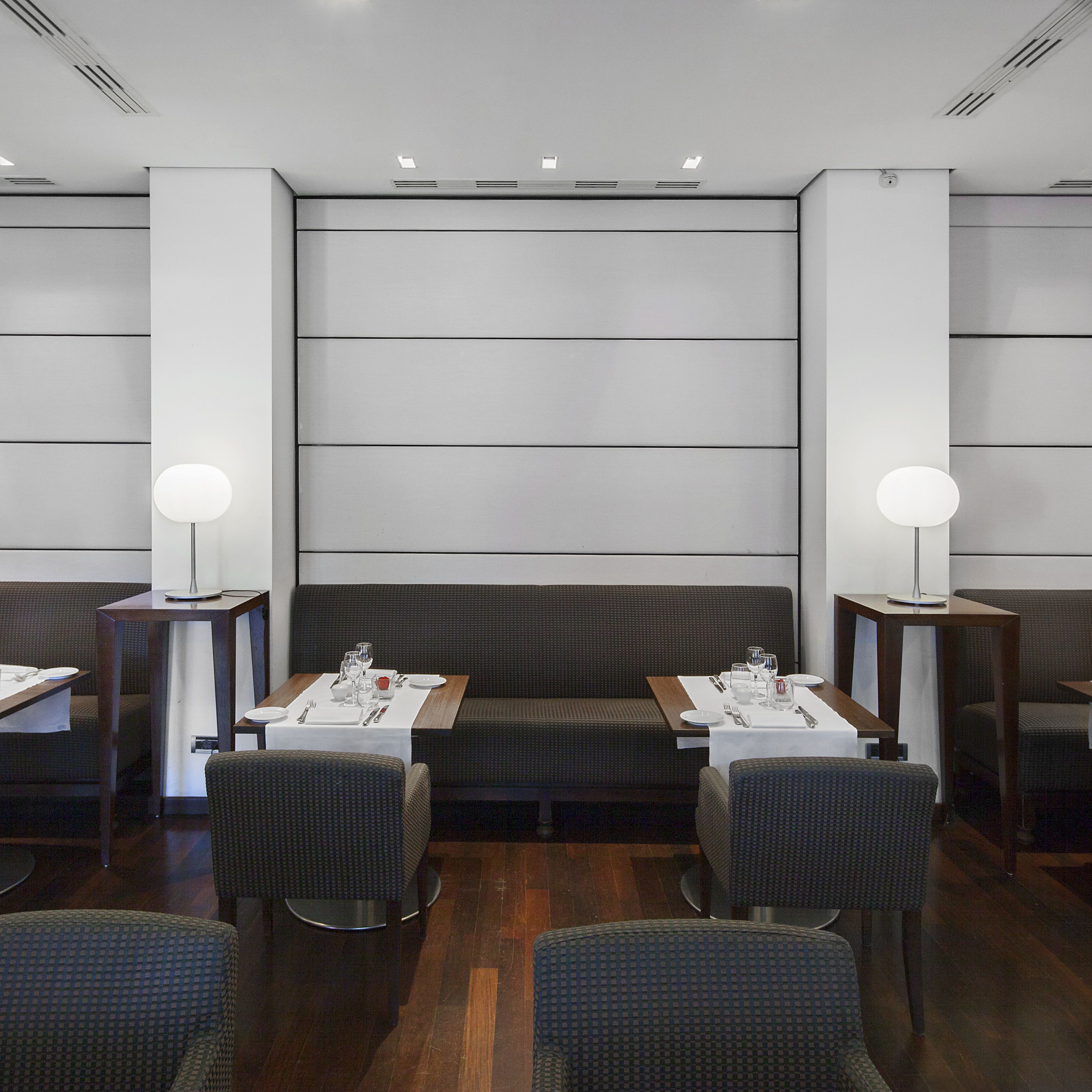 A modern dining area with a central booth and two smaller tables, each with a lamp and set table.