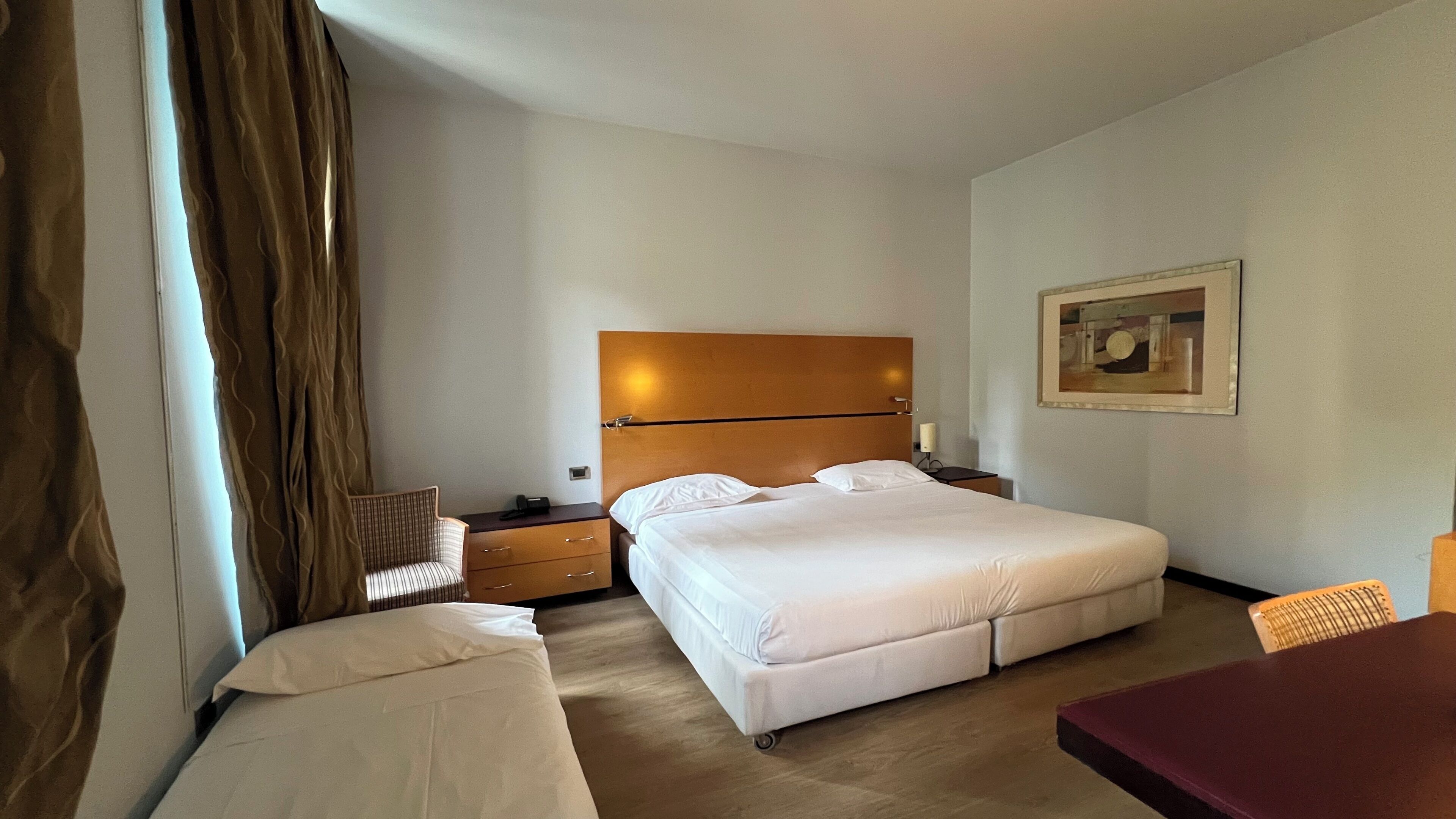 Una habitación de hotel con una cama, una silla, un escritorio y un cuadro en la pared.