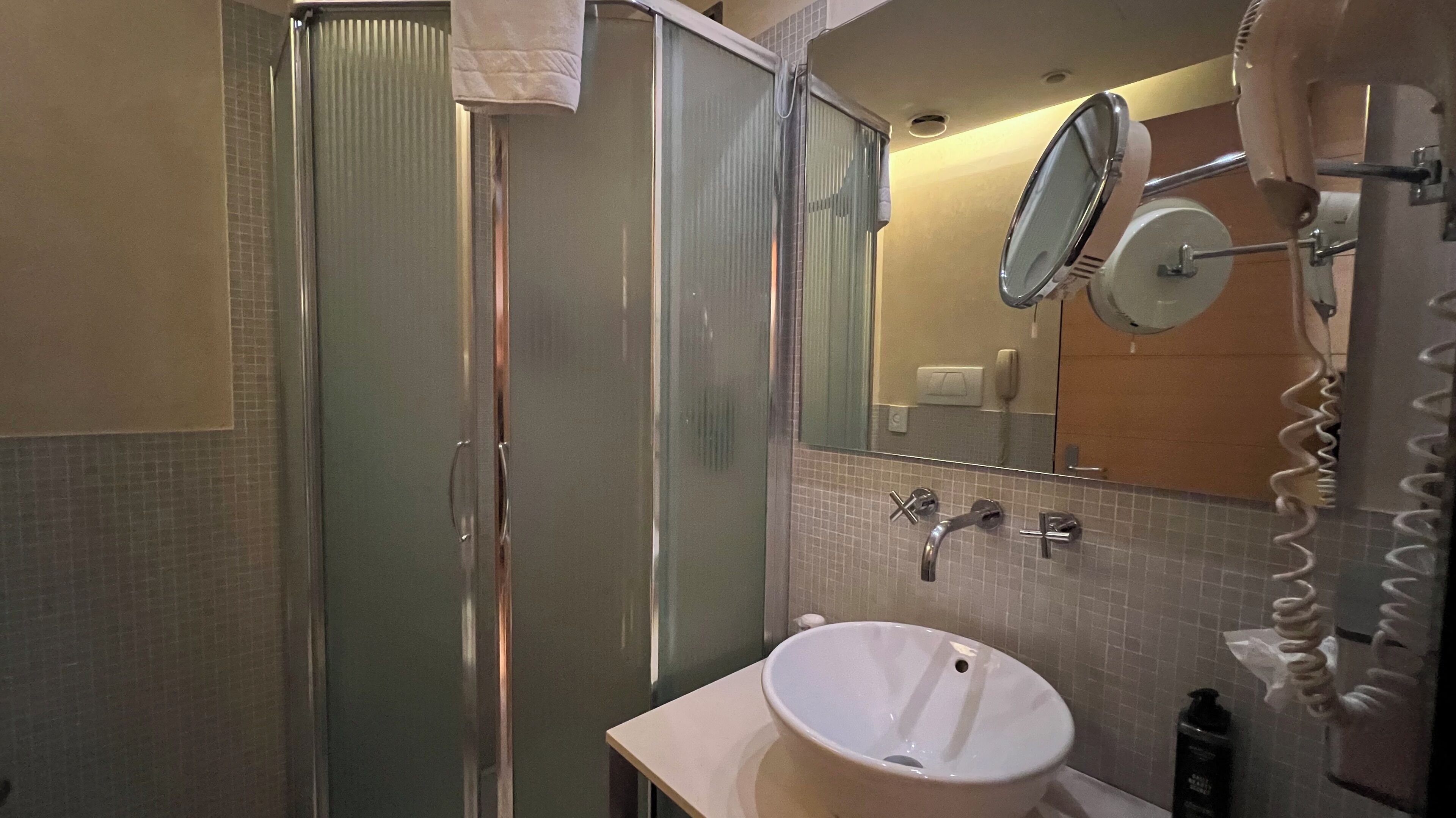 A bathroom with a glass shower enclosure, a white sink, a mirror, and a towel rack.
