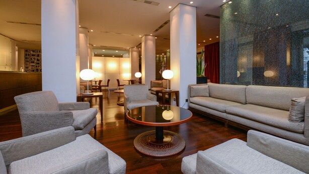 A modern lobby with a round table, sofas, and chairs arranged for guests. - Hotel Igea (Brescia)