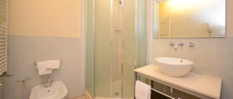 A bathroom with a glass-enclosed shower, a sink, and a mirror.