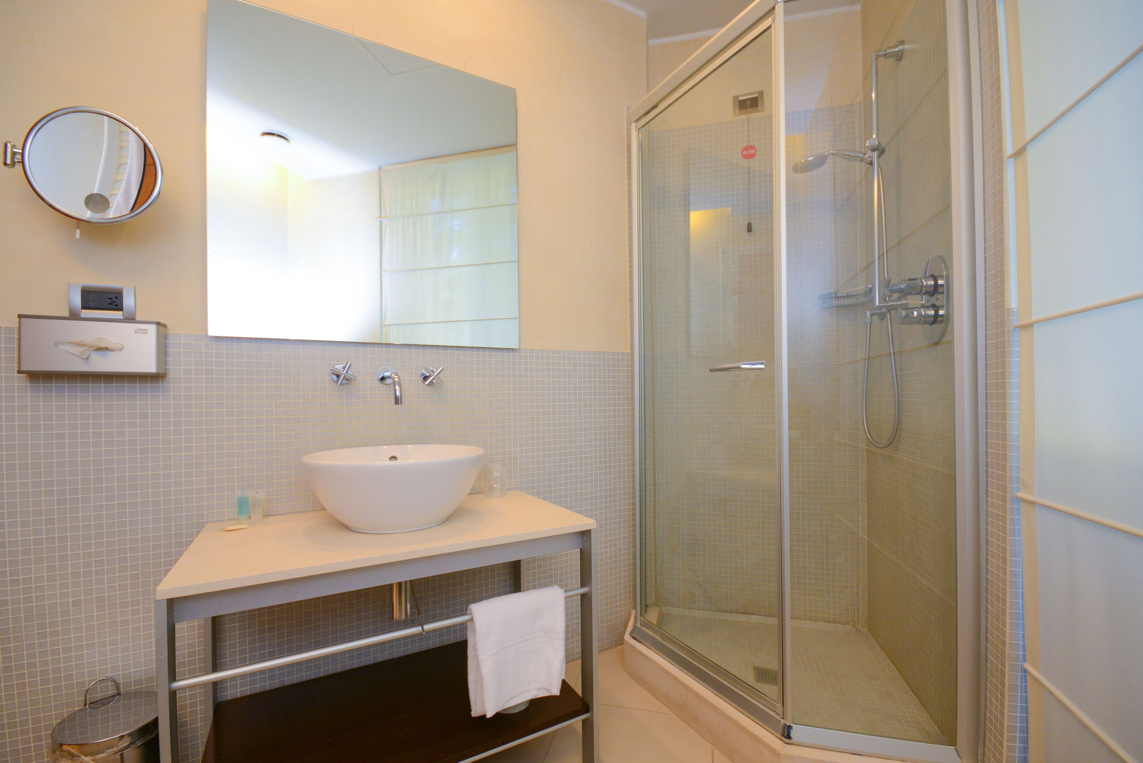 Un baño moderno con un espejo grande, un lavamanos blanco, una ducha con mampara de vidrio y un perchero para toallas.
