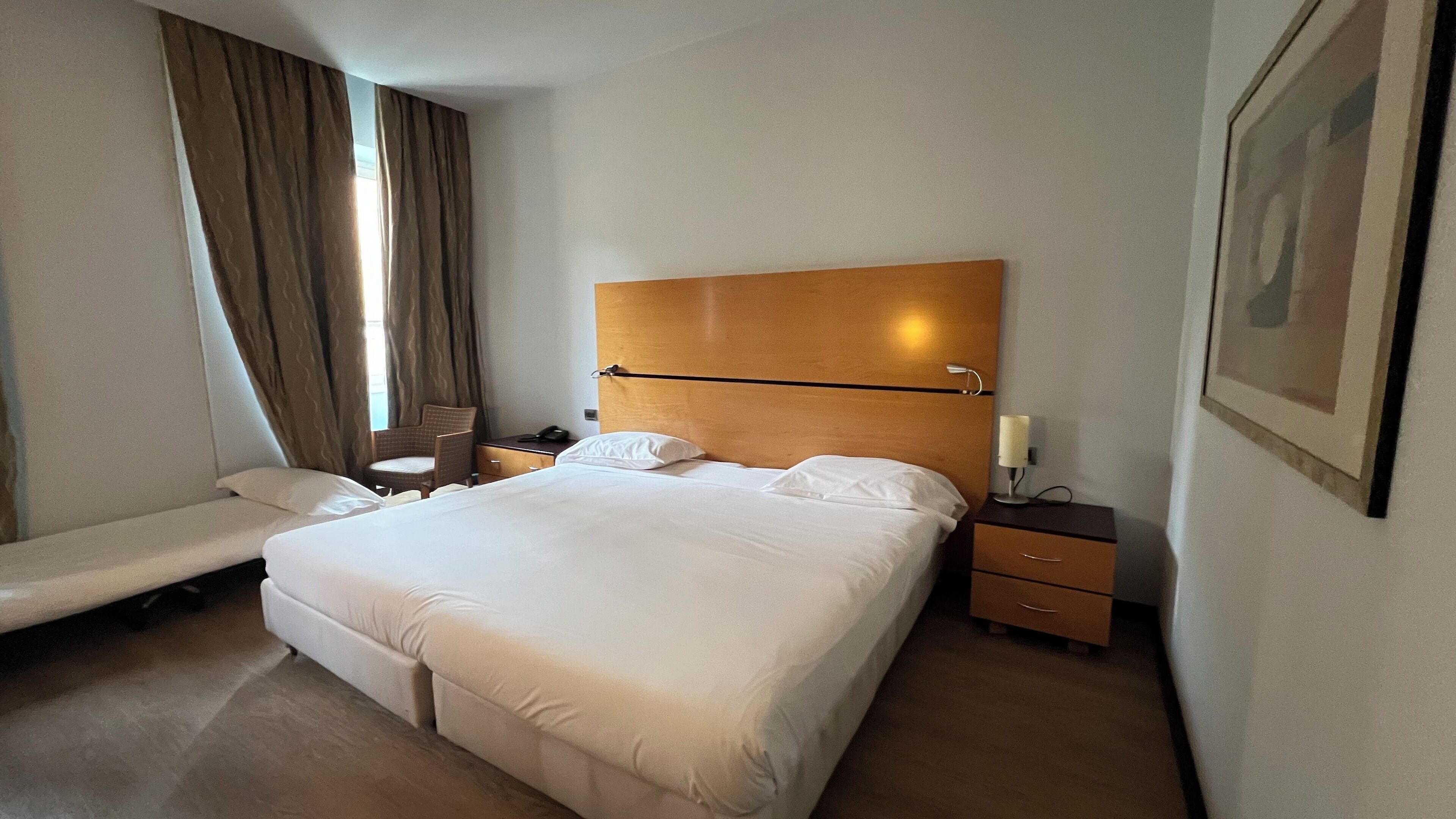 A hotel room with a large bed, a chair, a bedside table with a lamp, and a framed picture on the wall.