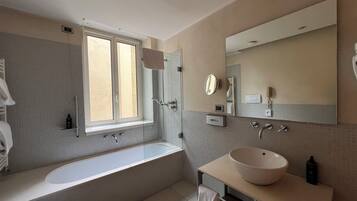 Een moderne badkamer met een groot bad, een wastafel met een waskom, een douche met glazen deur en een grote spiegel.