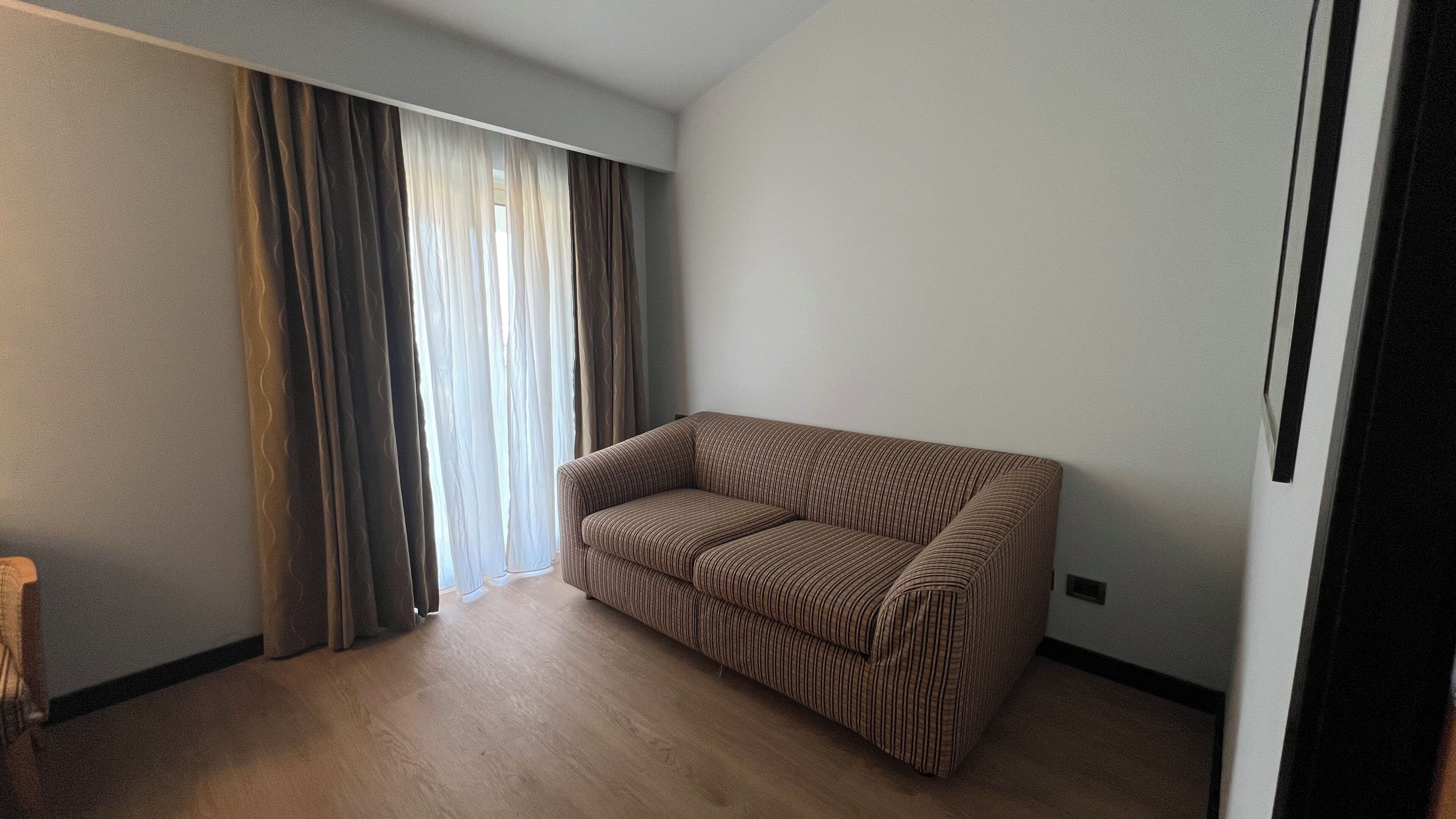 Een kamer met een gestreepte bank, een groot raam met gordijnen en een houten vloer.