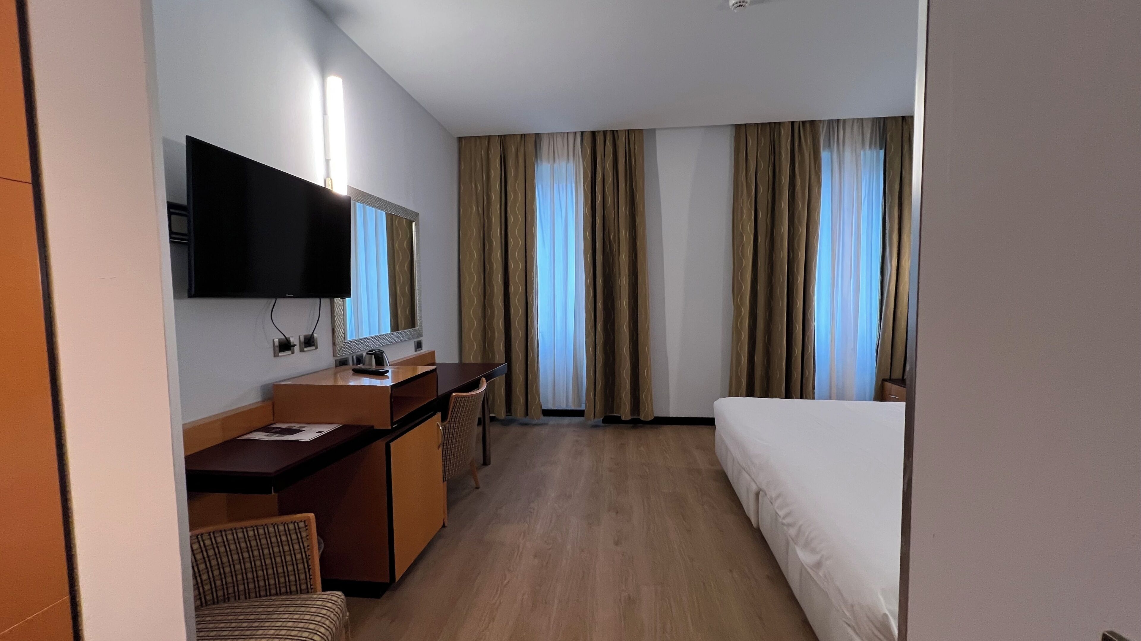 Une chambre d’hôtel équipée d’un lit, d’un bureau, d’une chaise, d’une télévision et de rideaux.