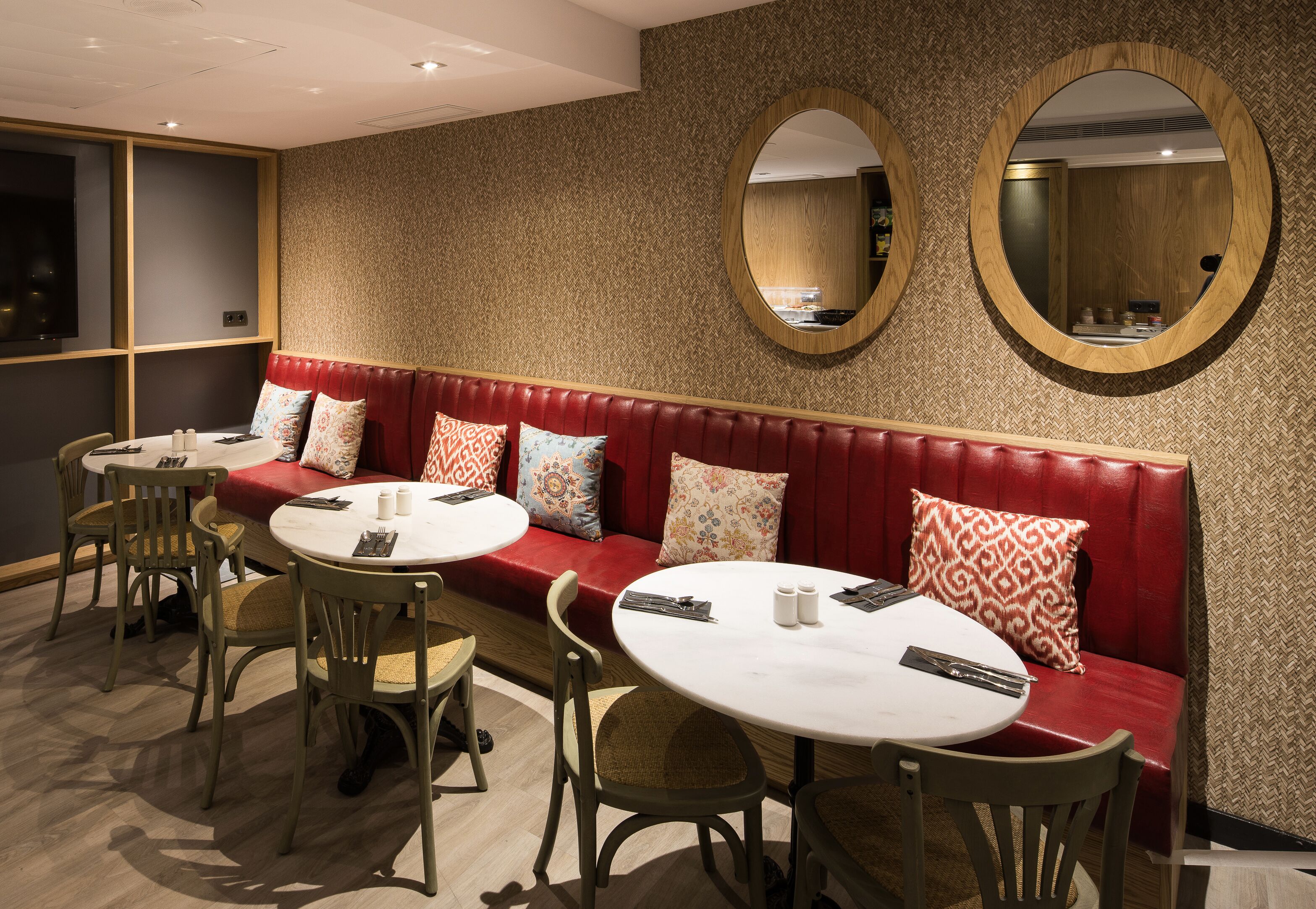 A dining area with a red leather booth, round tables, and chairs. There are two large mirrors on the wall.