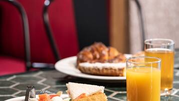 Una mesa con un plato de comida que incluye un sándwich, fruta y un croissant, junto con dos vasos de jugo de naranja.