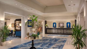 A spacious lobby with a blue patterned carpet, a reception desk, and decorative plants.