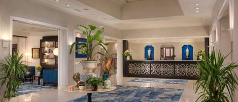 A spacious lobby with a blue patterned carpet, a reception desk, and decorative plants.