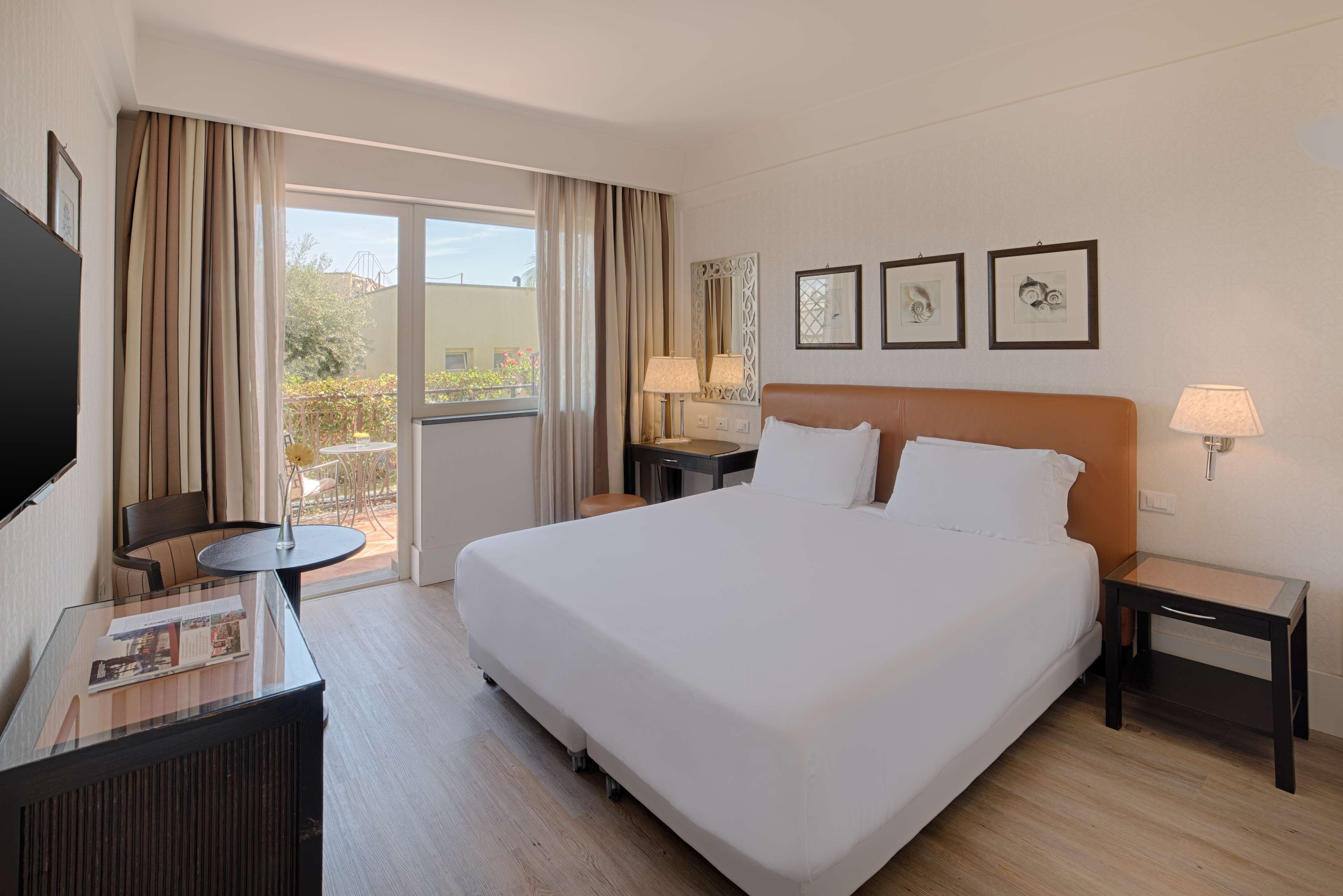 Una habitación de hotel con una cama grande, un escritorio con una silla, un televisor y un balcón con cortinas.