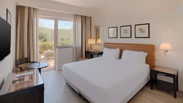 Una habitación de hotel con una cama grande, un escritorio con una silla, un televisor y un balcón con cortinas.