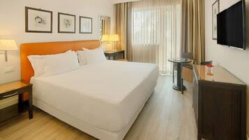 Una habitación de hotel con una cama grande, un escritorio con lámpara, televisión y cuadros en la pared.