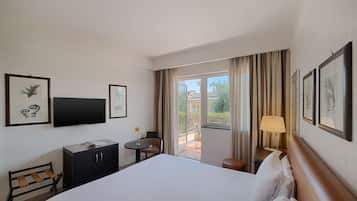 A hotel room with a large bed, a desk with a chair, a small table with a lamp, and a view of the outdoors.
