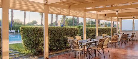 Un patio exterior con mesas y sillas, vista a la piscina y una siega.