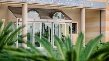 De ingang van hotel NH Parco degli Aragonesi met een glazen deur en een bord erboven.