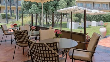 An outdoor patio with round tables and chairs, potted plants, and umbrellas.