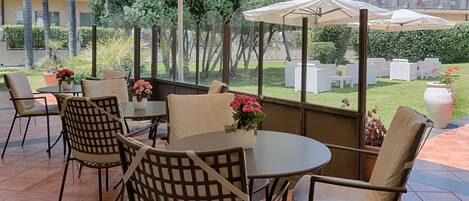 An outdoor patio with round tables and chairs, potted plants, and umbrellas.