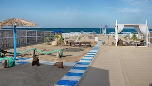 A beachside area with a wooden deck, lounge chairs, and a thatched umbrella.