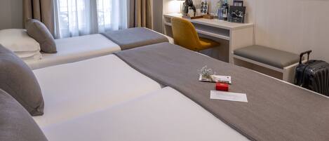A hotel room with two beds, a desk, a chair, a TV, and a suitcase.